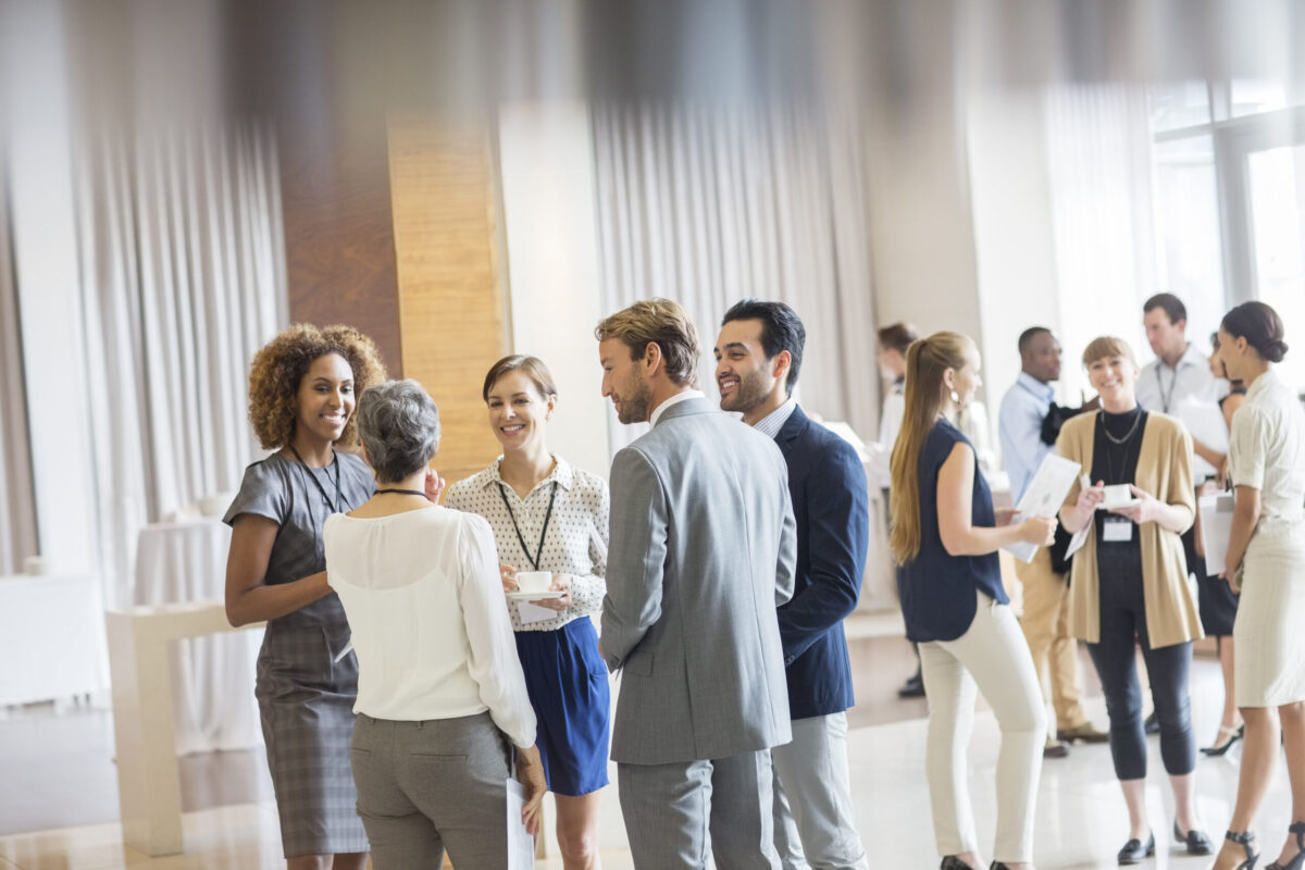Group Of Business People Standing In Hall, Smiling And Talking Together