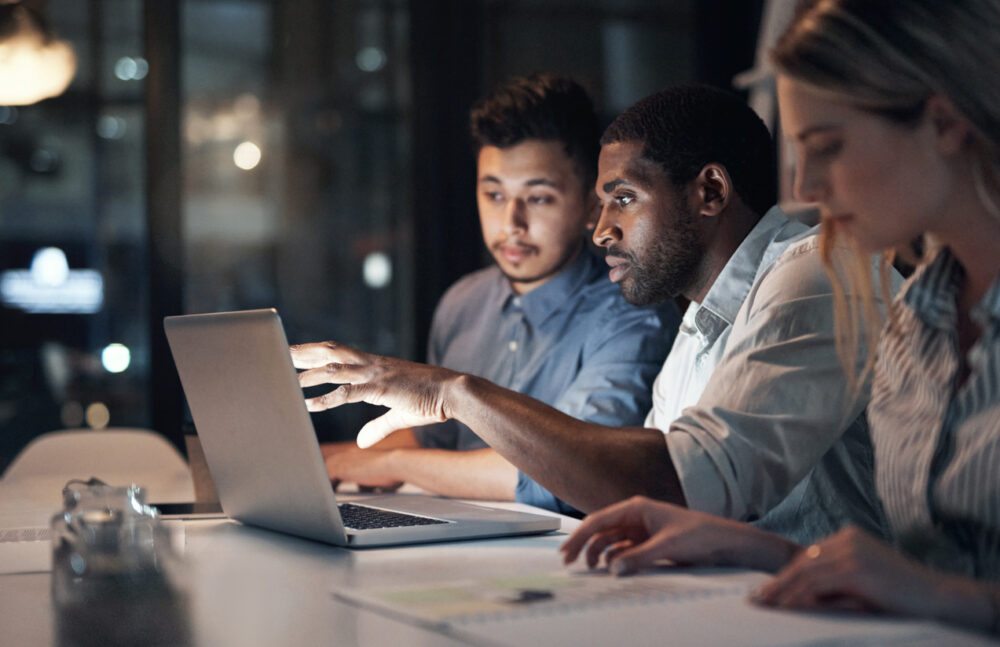 Shot of a team of young businesspeople using a laptop during a late night meeting in a modern office