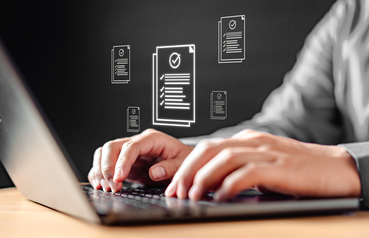 A person is typing on a laptop with a screen displaying a stack of papers.